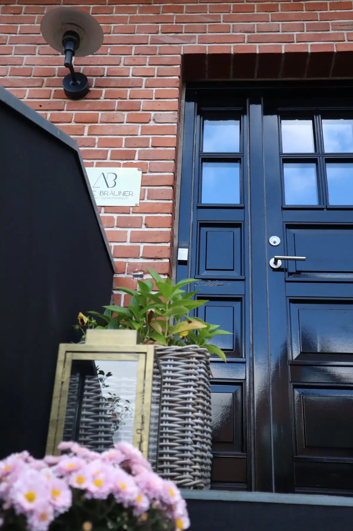 Hoveddør med skilt og blomster ved klinikken