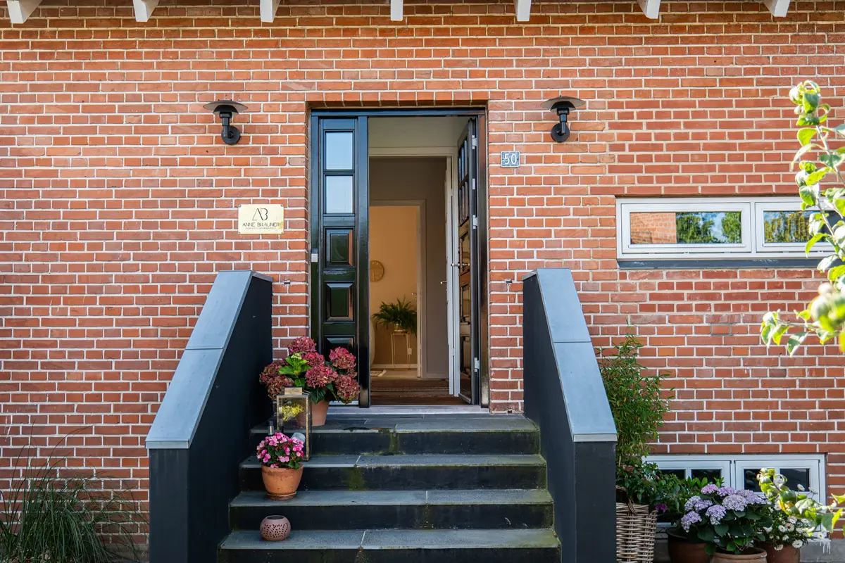 Indgangen i rødt murværk med trappe og blomster