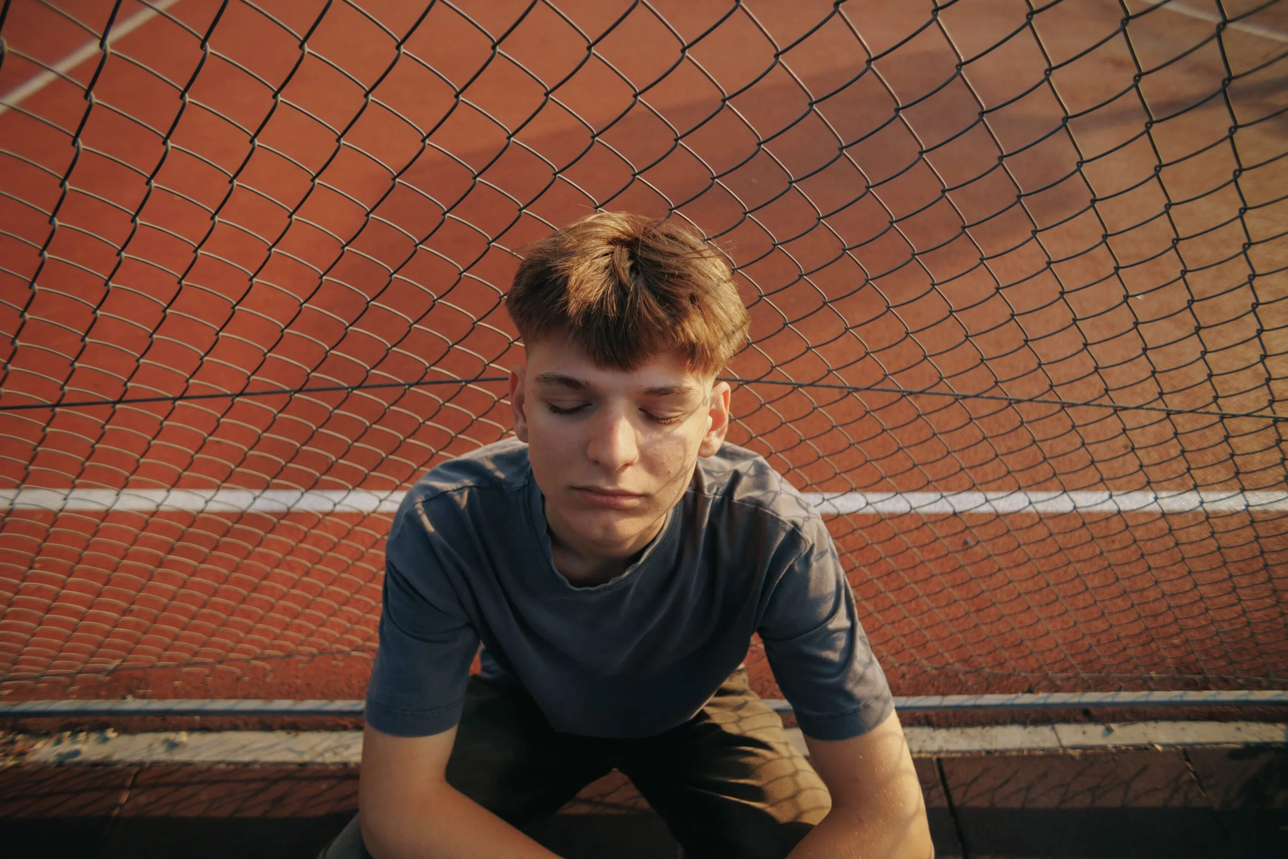 Person læner sig mod hegn på tennisbane